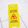 Bright yellow caution wet floor sign on white tiled floor indoors.