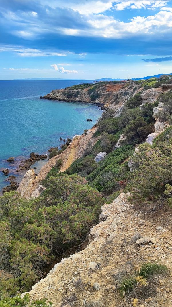 Breathtaking coastal cliff with lush greenery and clear blue sea under a vibrant sky.