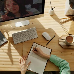 A student taking notes during a video call for online learning at home.