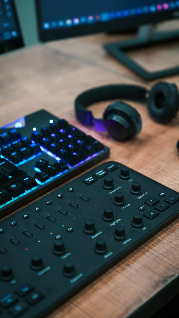 Close-up of a tech-savvy workspace featuring a keyboard, headphones, and sound mixer on a desk.