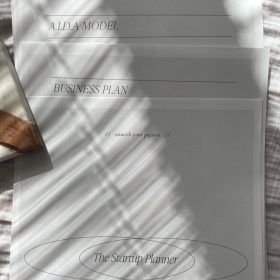 A stack of business documents with sunlit shadows, featuring a startup planner.