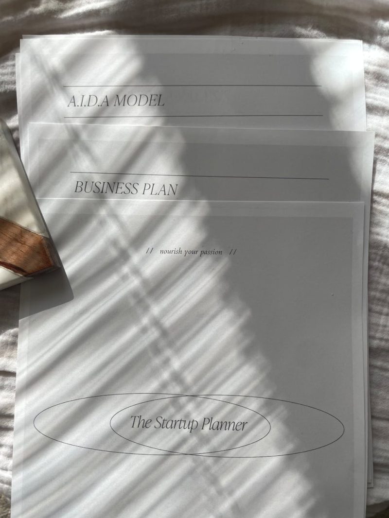 A stack of business documents with sunlit shadows, featuring a startup planner.