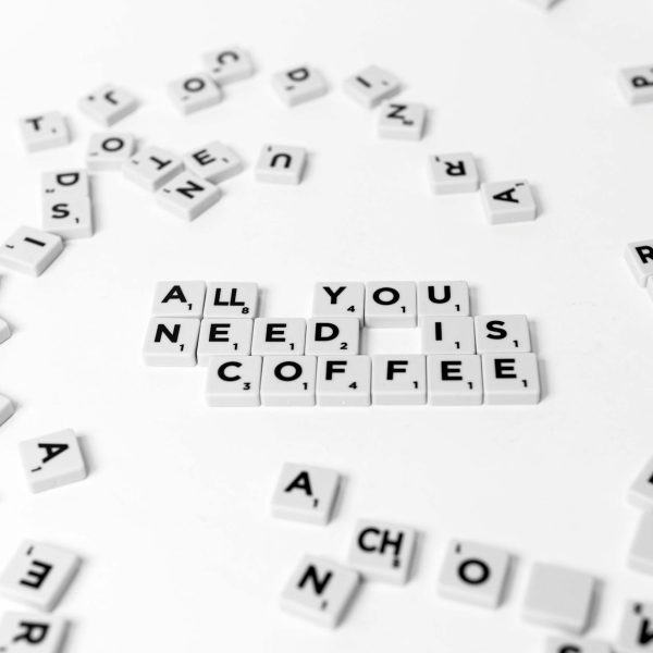 Scrabble tiles spell out 'All You Need Is Coffee' on a white background, offering a creative still life.