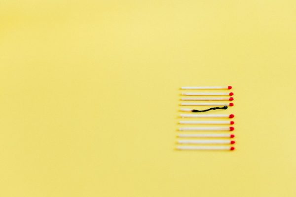 A conceptual image of burnt match among unlit ones on a yellow background, symbolizing uniqueness or burnout.