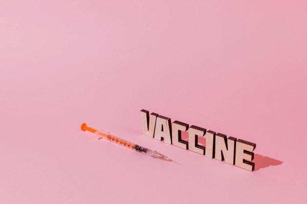 Syringe and 'Vaccine' text on pink background, conceptualizing healthcare and immunization.