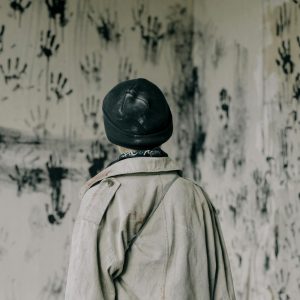 A person stands in a haunting room filled with black handprints, evoking a sense of mystery and fear.