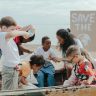 A group of children volunteering to clean a beach with a 'Save the Earth' sign.
