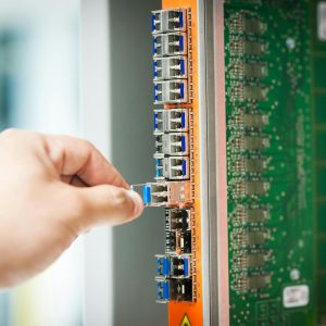 An individual connecting a cable into a network server port indoors, focusing on technology setup.