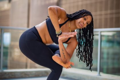 A woman practicing yoga outdoors on a mat with urban skyscrapers in the background.