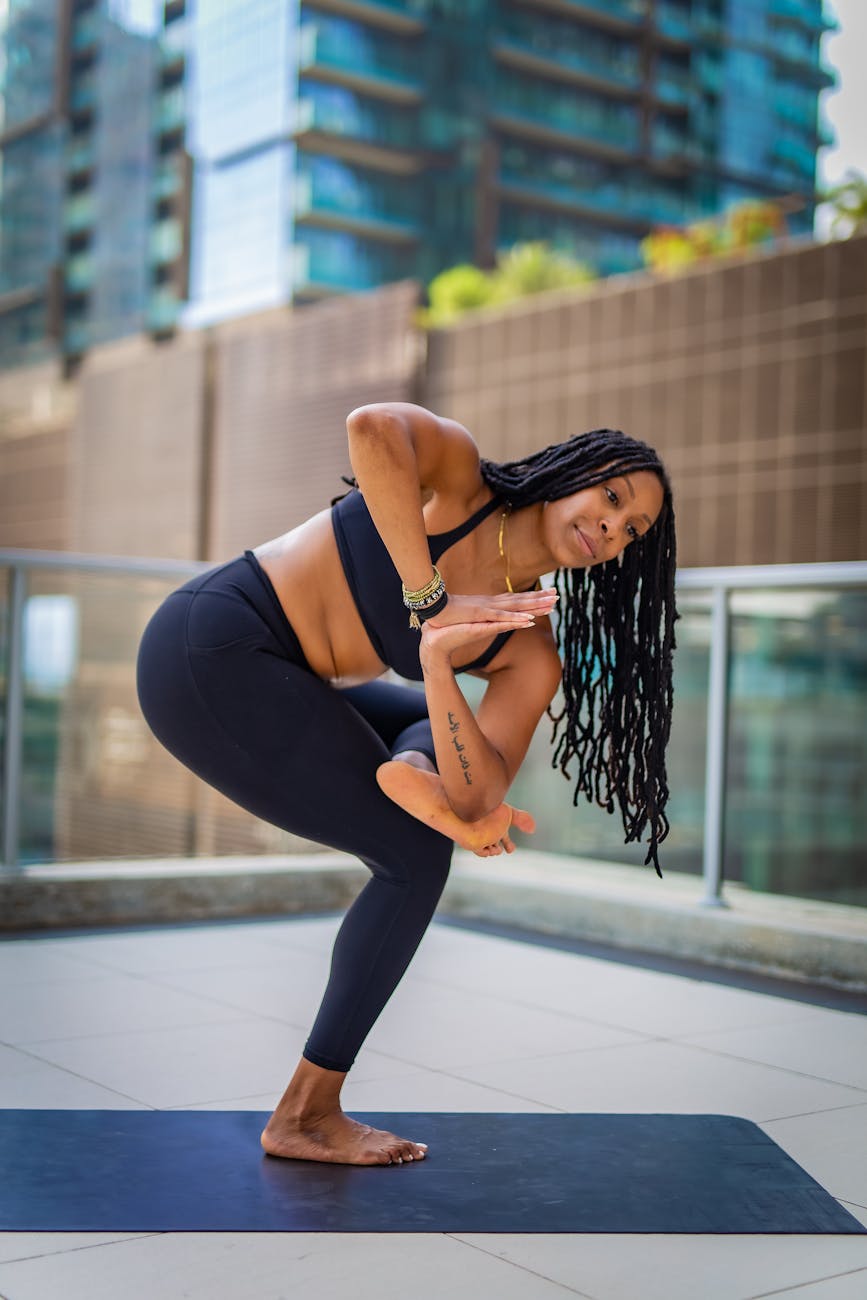 A woman practicing yoga outdoors on a mat with urban skyscrapers in the background.