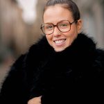 Cheerful woman with glasses and bun hairstyle wearing a winter coat. Outdoor portrait.