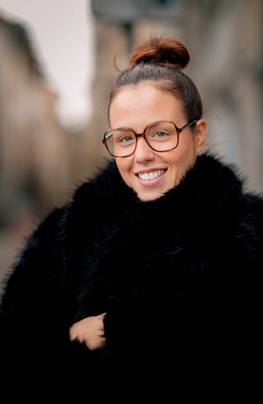 Cheerful woman with glasses and bun hairstyle wearing a winter coat. Outdoor portrait.