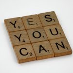 Wooden Scrabble tiles on white surface spelling 'Yes You Can,' promoting positivity and motivation.