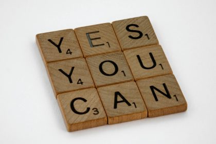 Wooden Scrabble tiles on white surface spelling 'Yes You Can,' promoting positivity and motivation.