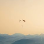A paraglider soars gracefully over the misty, layered mountains at sunset, capturing serene adventure.