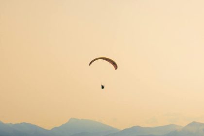 A paraglider soars gracefully over the misty, layered mountains at sunset, capturing serene adventure.