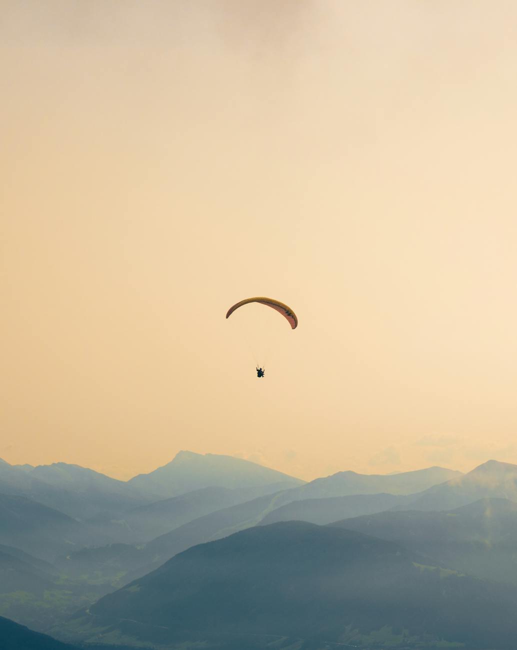 A paraglider soars gracefully over the misty, layered mountains at sunset, capturing serene adventure.