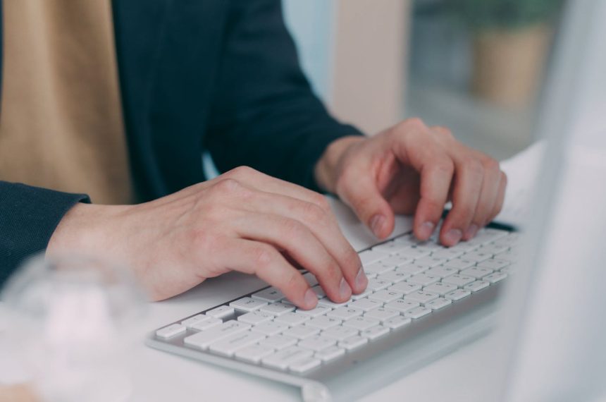 Close-up of hands typing on a white keyboard in an office setting. Ideal for business or technology themes.