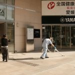 Two people clean the pavement outside a Yamaha building in Japan. Urban maintenance scene.