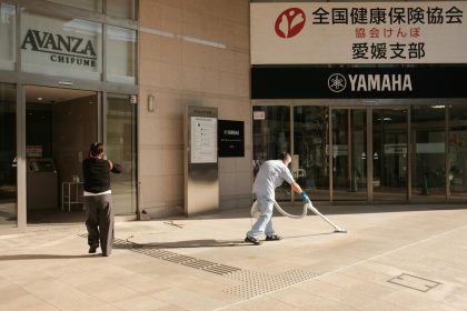 Two people clean the pavement outside a Yamaha building in Japan. Urban maintenance scene.