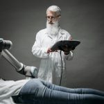 A scientist controls a robotic arm conducting research on a person lying down.