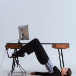 Woman in an innovative stretch position under an office desk, blending flexibility with workplace setting.