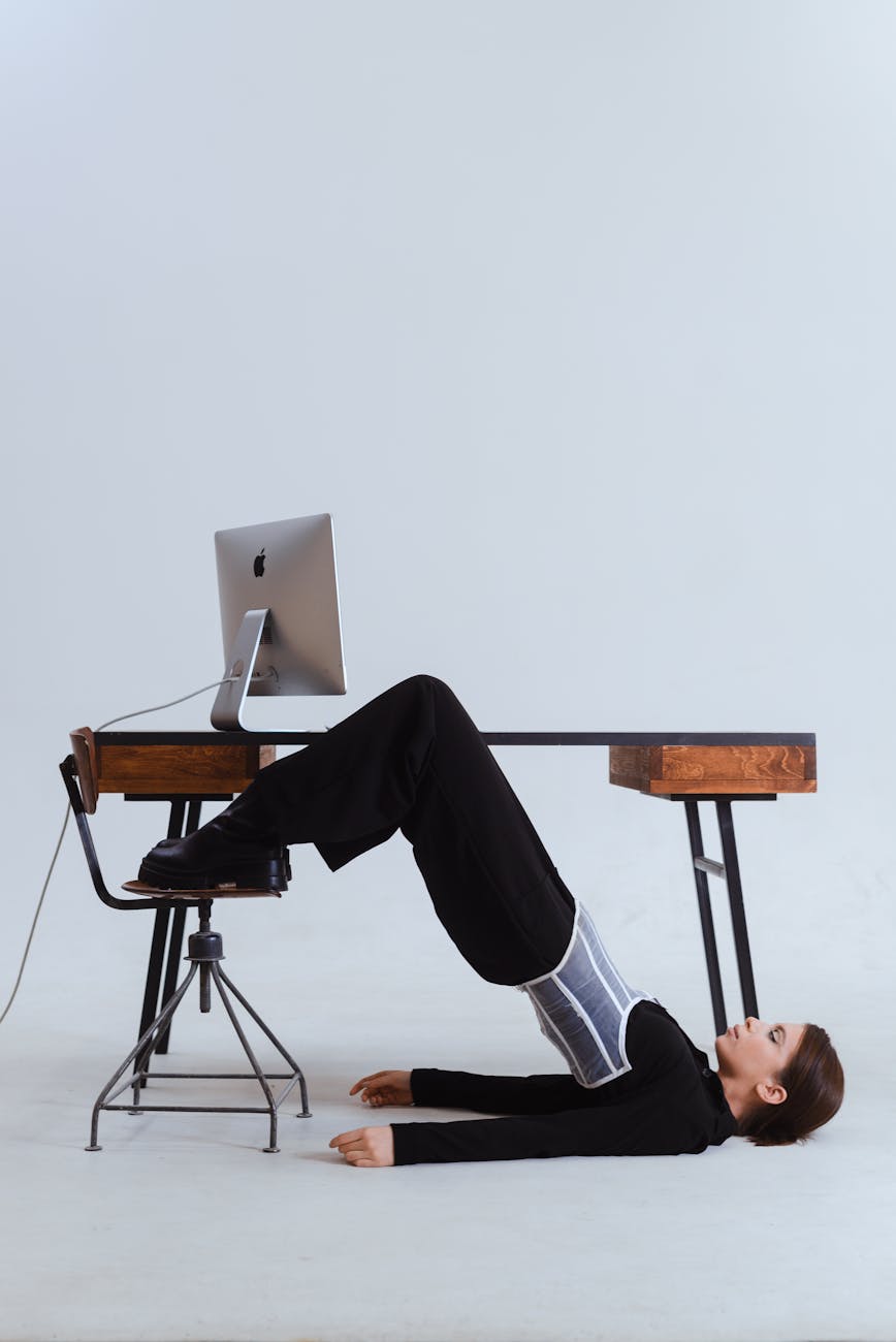 Woman in an innovative stretch position under an office desk, blending flexibility with workplace setting.