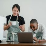 Two baristas enjoying work, actively collaborating and smiling together in a coffee shop.