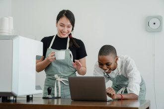 Two baristas enjoying work, actively collaborating and smiling together in a coffee shop.