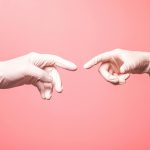 Close-up of hands in surgical gloves reaching out against a pink background.