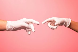 Close-up of hands in surgical gloves reaching out against a pink background.