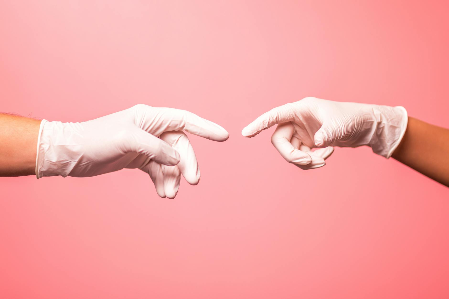 Close-up of hands in surgical gloves reaching out against a pink background.