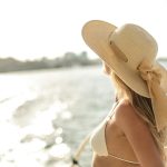 Back view of slim female in bikini top and straw hat enjoying trip on cruise boat on sunny day while relaxing during summer vacation and looking away