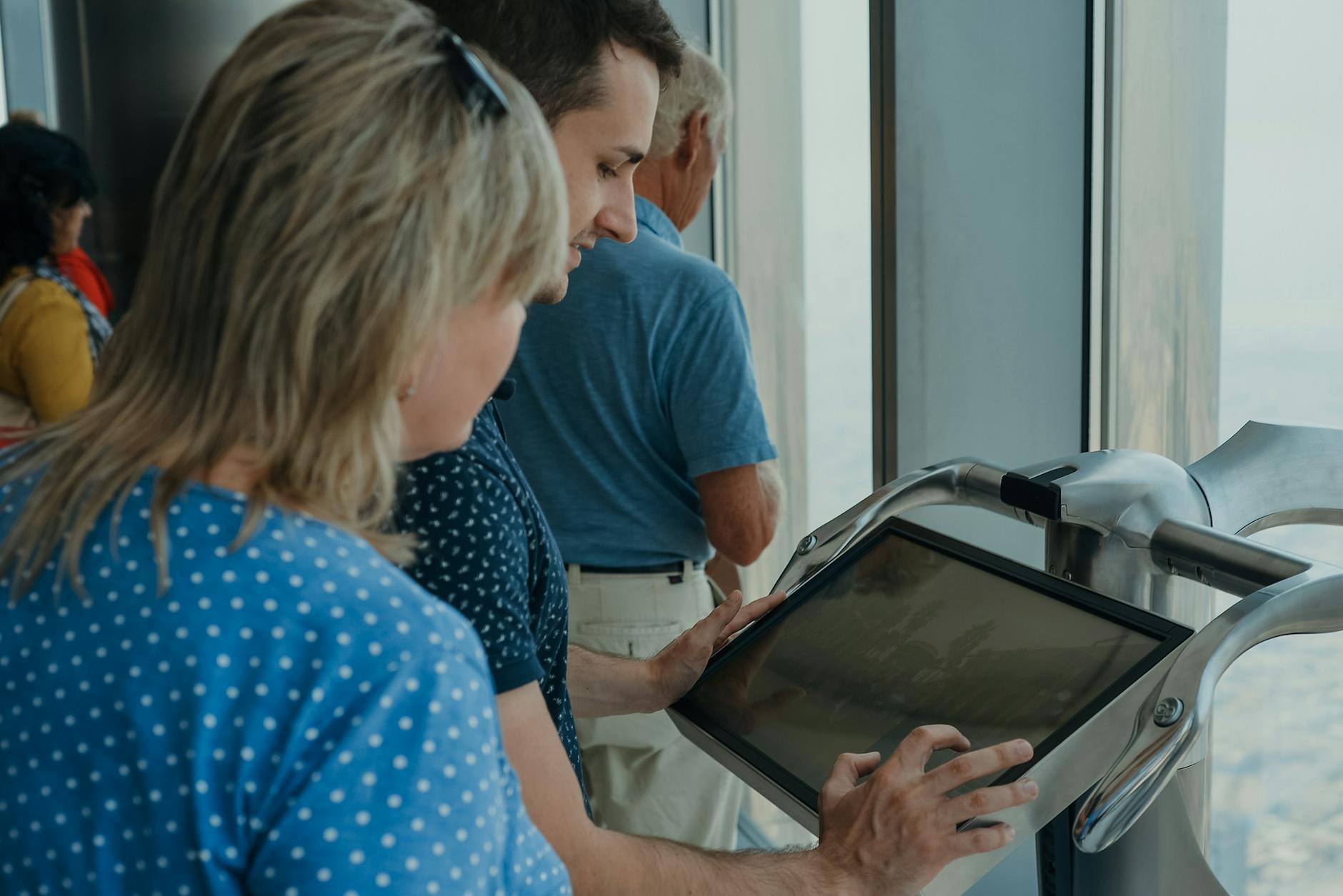 Tourists explore an interactive display at an observation deck, offering panoramic city views.