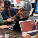 Diverse team collaborating with laptops in a modern office setting, discussing digital evolution.