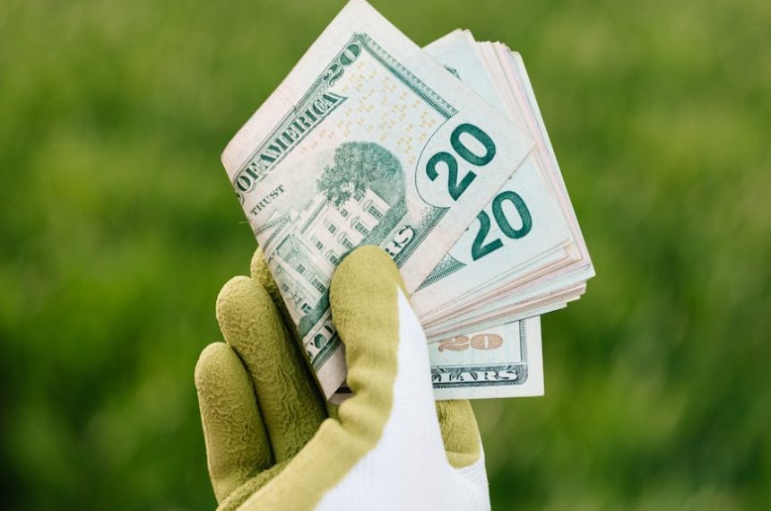 Gloved hand displaying twenty dollar bills with green field background.