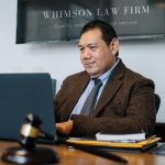 A lawyer working on a laptop in a legal office, wearing a suit and tie, with a gavel on the desk.
