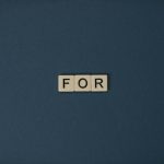 Artistic display of Scrabble tiles spelling the word 'For' on a dark background.