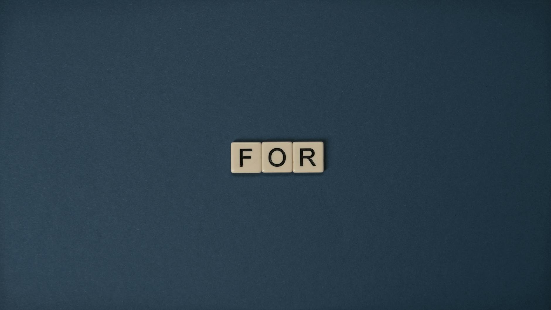 Artistic display of Scrabble tiles spelling the word 'For' on a dark background.