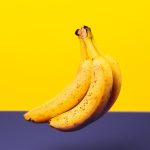 A bunch of fresh bananas isolated against a vibrant yellow and purple background.